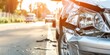 Close-up of a car's smashed front after a traffic collision, with sunlit road and vehicles in background.