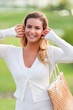 Smiling young woman pulling hair back oudoors in white cardigan sweater