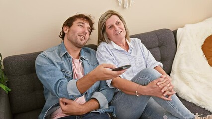 Poster - Mother and son in joyful expression, sitting comfortably together on a sofa at home, happily watching tv, their bonding time showcasing the love of family.