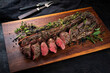 Traditionally roasted saddle of venison with fillet pieces and herbs served as close-up on a wooden design cutting board and a carving set