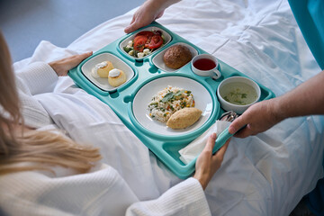 Nursing assistant serving meal to recumbent patient