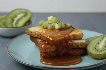 Wall Mural - Healthy breakfast at the hotel. Toast with honey and pieces of fruit and kiwi on grey background