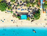 Fototapeta Góry - Aerial view of pool, white sandy beach with palms, umbrellas, swimming people, boat, blue ocean, at sunset. Summer vacation in Nungwi, Zanzibar island. Tropical landscape. Clear azure sea. Top view