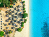 Fototapeta Do pokoju - Aerial view of green palm trees, umbrellas on the empty sandy beach, blue sea at sunset. Summer travel in Nungwi, Zanzibar island. Tropical landscape with palms, white sand, clear ocean. Top view