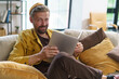 A man in a yellow jacket is sitting on a couch with a tablet in his lap. He is smiling and he is enjoying his time