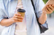 A woman is holding a coffee cup and a cell phone. She is wearing a blue shirt and a black backpack