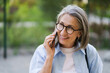 A woman wearing glasses is talking on her cell phone. She is smiling and she is in a good mood