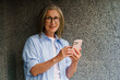 A woman in a blue shirt is holding a cell phone. She is smiling and she is happy