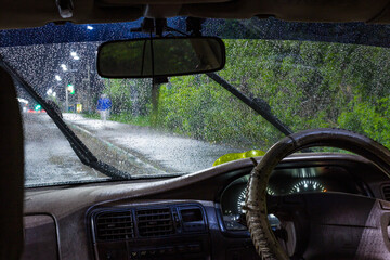 Wall Mural - view from the inside of a working car at night on an illuminated road during heavy rain and thunderstorms, the danger of driving in poor visibility on highways in big cities