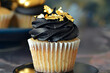 A cupcake with jet black frosting and a contrasting bright, edible gold leaf design, creating an elegant and luxurious birthday treat.