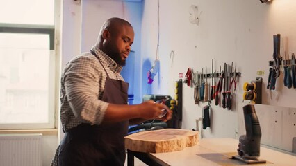 Wall Mural - Carpenter inspecting wood in assembling shop, putting safety glasses on and picking tool from rack. Woodworking specialist in studio picking lumber block and carving gear for it, camera B