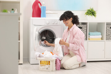 Canvas Print - Happy woman putting laundry into washing machine indoors