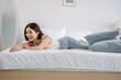 © JR-50 - A woman in casual wear stretches with a smile, lying on a white bed, enjoying a moment of relaxation