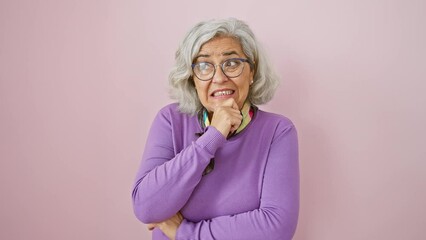 Sticker - Nervous middle age woman, grey-haired and bespectacled, standing worried over a tough question, hand on chin, isolated on a pink background