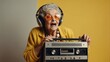 © muqadas - funny granny in hipster clothes listening to music on a tape recorder and showing a kiss on a yellow isolated background, elderly cool woman dancing at a party and having fun