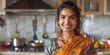 Assured, attractive Indian woman smiling at camera in kitchen at home. Joyful, lovely Hindu homemaker in India indoors, close-up portrait.