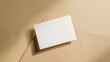 Blank white card propped up against a beige wall with shadow detail.