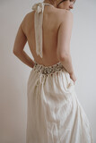 Fototapeta Tulipany - Back view of young woman in neutral cream beige evening dress against white wall. Minimal chic fashion concept
