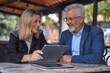 © SerPak - A happy mature couple is interacting with a digital tablet while sitting at an outdoor cafe setting