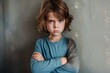 A young child with tousled hair shows a sulky expression and crossed arms, conveying a moody atmosphere