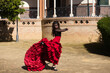 Beautiful woman dancing flamenco in Seville, Spain. She wears a red and black dress typical of a flamenco dancer with a lot of art, you can see the movement in the air of the frilly dress.