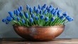   A copper bowl holding blue flowers sits atop a wooden table against a wall