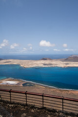 Wall Mural - Island of La Graciosa from the viewpoint of El Rio. Turquoise ocean. Blue sky with big white clouds. Caleta de Sebo. Village. volcanoes. Railing of the viewpoint. Lanzarote, Canary Islands, Spain