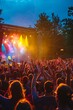 A bustling crowd at an outdoor concert, hands raised, faces lit by colorful stage lights, and the energy of the music