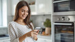 beautiful happy girl with a smile on her face stands in her modern kitchen and holds a smartphone in her hands