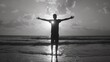 A man stands with his arms outstretched on the beach sunset, silhouette style, monotone black-white