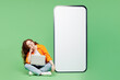 © ViDi Studio - Full body young IT woman wear orange shirt white t-shirt casual clothes big huge blank screen mobile cell phone smartphone use laptop pc computer isolated on plain green background. Lifestyle concept.