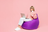 Fototapeta  - Full body elderly IT woman 50s years old wear sweater shirt casual clothes glasses sit in bag chair hold use work on laptop pc computer waving hand isolated on plain pink background Lifestyle concept