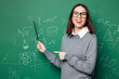 © ViDi Studio - Young teacher woman she wears grey casual shirt glasses hold pointer indicate on formula look camera isolated on green wall chalk blackboard background studio Education in high school college concept