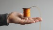 A close-up of a hand holding a Basant kite spool, the thread standing out against the white background