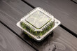 © Sergey - Plastic container with sunflower microgreens closed and sealed on a wooden background.