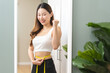 Loss weight slim, smile asian young woman, cheerful girl measuring waist size with tape measure, wear in fit sport, looking reflect in mirror at home. Fitness shape slender for wellbeing healthcare.