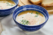 Two bowls of creamy potato soup, spoons, napkin and wooden cutting board with a loaf of bread and cut pieces. The surface of the soup is decorated with cream, croutons, parsley and ground red pepper.