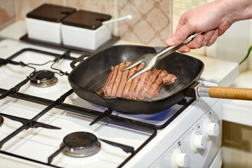 Wall Mural - The process of cooking two beef steaks in frying pan, the hands of male chef salting raw meat, close-up