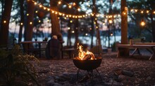 Cast Iron Fire Pit Campfire Place At Forest Beach Camping With Brgiht Burning Flame At Evening Time Against Light Bulb Garland And Trees.