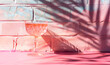 Crystal glass with cold alcohol drink, pastel pink painted brick wall, tropical leaf shadows, summer holiday, posh party.