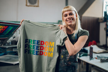 Smiling print shop worker showing silkscreen printed t-shirt at camera