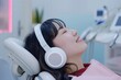 © Elena - Asian female patient wearing headphones in a dental chair looking relaxed