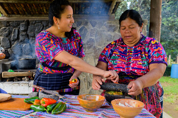 Canvas Print - Two adult Mayan women talk while grinding the vegetables that will be used to season the broth.