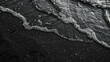 A top view and flat lay of a black sand beach with waves and foam.