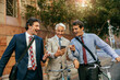© Marko Geber - Three businessmen in suits looking at a smartphone together outdoors with bicycles