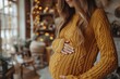 A young, expectant mother caresses her pregnant belly, dressed in a cozy yellow sweater, standing in a warmly lit, festive room with bokeh lights in the background