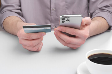 Canvas Print - Online payment. Man with smartphone and credit card at light grey table, closeup