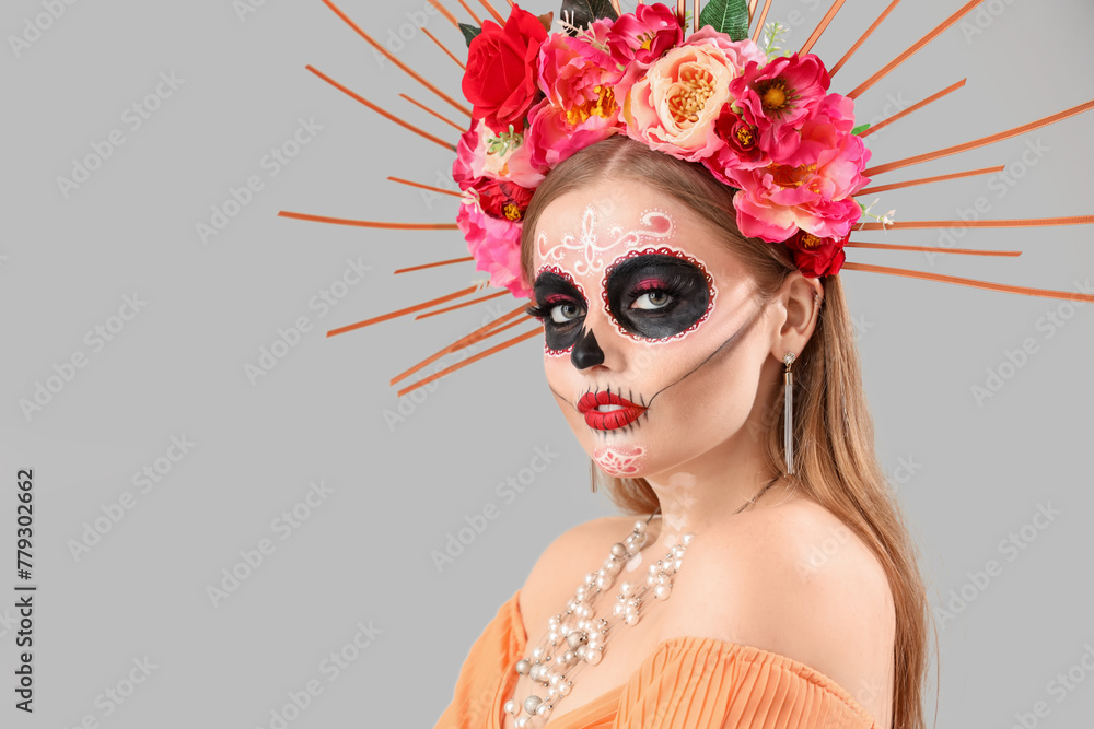 Young woman with painted skull on her face against grey background. Celebration of Mexico's Day of the Dead (El Dia de Muertos)