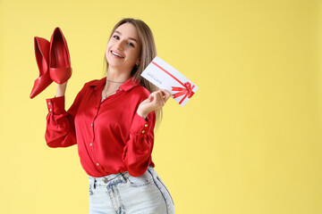 Sticker - Happy young woman with gift card and heels on yellow background