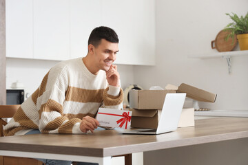 Poster - Young man with gift card and laptop shopping online in kitchen